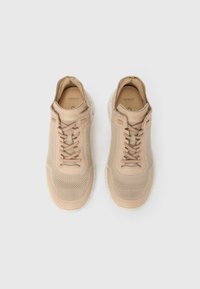 Ζεύγος μπεζ πλεκτών αθλητικών παπουτσιών με κορδόνια και μαλακές σόλες, εμφανιζόμενα από πάνω σε λευκό φόντο.