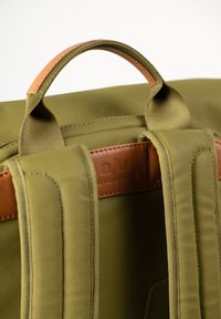 Zaino in tessuto verde oliva con dettagli in pelle marrone, dotato di spallacci imbottiti e superficie testurizzata.