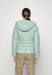 Padded mint green jacket with a hood, featuring quilted texture and elastic cuffs, worn over plaid patterned pants.