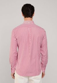 Rot-weiße gestreifte Langarmbluse mit einem Button-Down-Kragen und einem Faltendetail hinten. Die Manschetten haben Knopf-Akzente.
