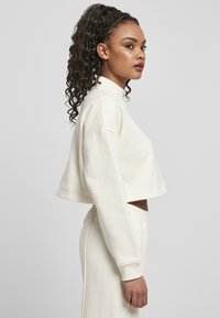 Beskyttende sweatshirt i myk kremfarge, med høy hals og lange ermer med ribbede mansjetter. Kombinert med matchende bukser.