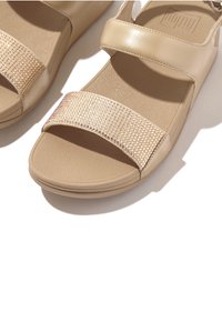 Tan sandalen met een gestructureerde zool en twee banden. De bovenste band is versierd met kleine, glanzende rhinestones voor extra detail.