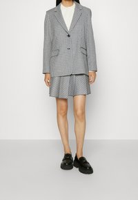 Blazer a cuadros en blanco y negro sobre una blusa blanca, combinado con una falda a juego con los mismos cuadros. Mocasin negro con suelas gruesas completan el look.