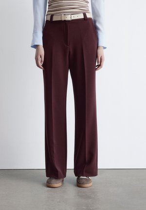 Maroon wide-leg pants with a smooth texture and front pockets, paired with a cream belt. Grey shoes with tan rubber soles.