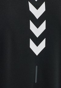 Sort stof med hvide chevronmønstre, der er arrangeret lodret. En lille grå accentlinje fremhæver bunden og tilføjer kontrast.