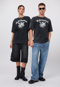 Sorte grafiske t-skjorter med teksten "Redemption", brukt med slitte svarte shorts og falmede blå jeans. Sorte støvler og sko fullfører antrekkene.