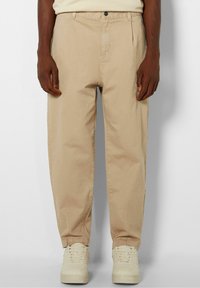 Beige bomullsh byxor med en avslappnad passform, framfickor och sidofickor. Kombinerat med krämfärgade sneakers. Minimalistisk design utan synliga mönster.