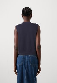 Tmavě modrý top bez rukávů s kulatým výstřihem, krátkým střihem a hladkou texturou. Kombinován s vysokým pasem džínové sukně s kapsami.