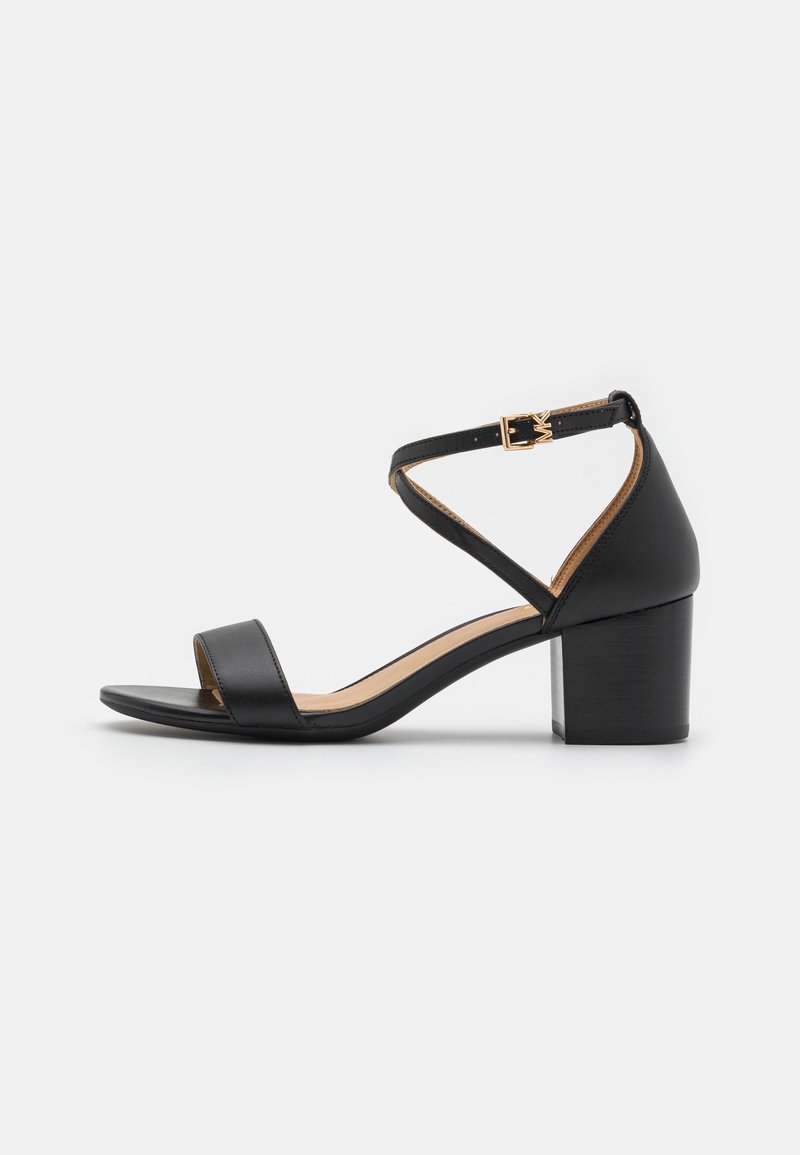 Sandale ouverte en cuir noir avec talon bloc, bride à la cheville et boucle dorée, vue de côté sur fond blanc.