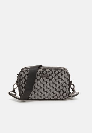 Bolso bandolera de tela gris con patrón de logotipo negro, cierre de cremallera, correa desmontable y detalles de herrajes metálicos. Forma rectangular compacta.