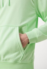 Hoodie verde claro, feito de material suave. Apresenta um bolso canguru à frente e punhos canelados. Textura suave, corte descontraído.