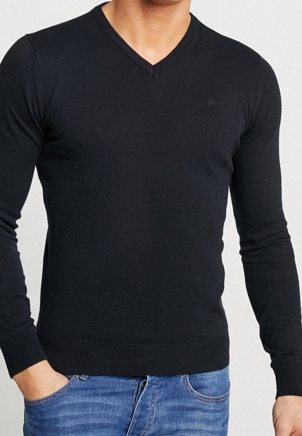 Schwarzer, figurbetonter Pullover mit V-Ausschnitt und langen Ärmeln; gerippte Bündchen und Saum; weiche Textur; getragen über blauen Jeans. Minimales Logodetail.