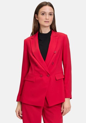 Red double-breasted blazer with peaked lapels, two front pockets, and matching trousers, crafted from textured fabric. Black turtleneck underneath.