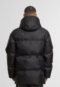 Svart boblejakke med høy krage og festet hette. Har quiltede seksjoner for isolasjon og en glatt, blank overflate.