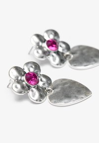 Sølvøredobber med et blomstermotiv, med teksturerte kronblad og en rosa edelsten i midten, festet til et hjerteformet anheng.