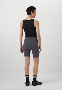 Top nero senza maniche con design a incrocio sulla schiena, pantaloni corti grigi aderenti con pannelli testurizzati e area imbottita per il sedere, abbinati a scarpe da ciclismo nere e calze.