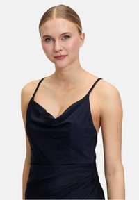 Marinblå silkig klänning med tunna band och en cowl-nek. Designen betonar draperade detaljer på bysten.