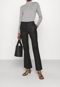 Czarne, skórzane spodnie o szerokich nogawkach zestawione z jasnoszarym, długim golfem. Modelka trzyma czarną torbę typu bucket i nosi czarne sandały na paskach.