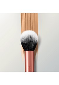 Make-upkwast met zwart-witte haren die een streep beige vloeibare foundation aanbrengt op een lichtgrijze ondergrond.