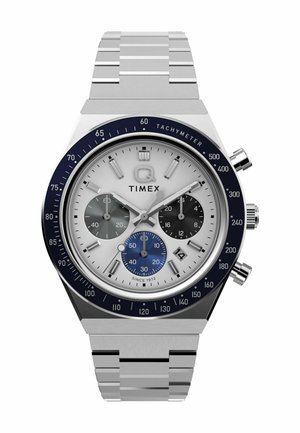 Srebrny zegarek ze stali nierdzewnej z białą tarczą, niebieską bezną tachymetryczną, trzema sub-tarczami oraz szczotkowanym metalowym paskiem. Wyróżniającą cechą jest okno daty.