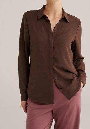 Hnědá košile s dlouhým rukávem, zapínáním na knoflíky vpředu, límečkem a hladkou texturou, doplněná růžovými kalhotami.