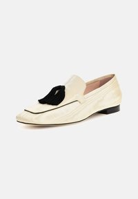 Kremowe pantofle wsuwane z teksturowanym wzorem, czarnym frędzlem i niskim obcasem. Obejmuje spiczasty czubek i obszywane wykończenie.
