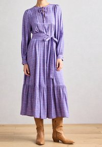 Lilla kjole med lange ærmer, blomsterprint, bindebånd i taljen og lagdelt nederdel, kombineret med brune ankelstøvler.