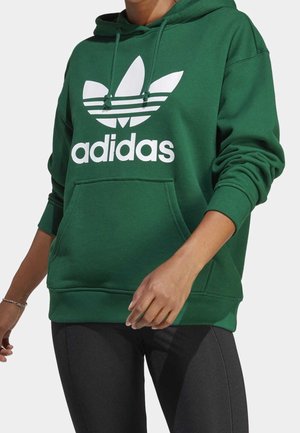 Zelená mikina vyrobená z bavlněné směsi, s velkým bílým logem Adidas a třípruhovými akcenty na hrudi, má přední kapsu.