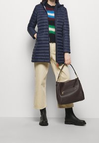 Marine pufferjack, meerkleurige gestreepte trui, beige wijde broek, zwarte rubberen laarzen en donkerbruin gestructureerde handtas met hardware.