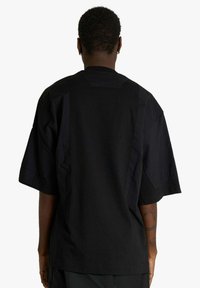 Camicia nera oversize a maniche corte con vestibilità rilassata, tessuto strutturato, scollo arrotondato e dettagli a pannello a contrasto.