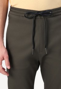 Olive green sweatpants with an elastic waistband, black drawstring, and side pockets. Smooth texture, fitted design, and minimal accents.
