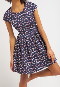 Granatowa sukienka z dopasowanym gorsetem i rozkloszowanym dołem, wykonana z lekkiego materiału w wzór kolorowych ptaków i kwiatowych akcentów.