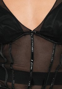 Fekete hálós felső mély V-nyakkal, fényes fekete részletekkel és vízszintes csíkokkal, valamint textúrált, félig átlátszó anyagból.