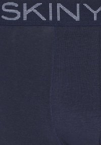 Granatowe męskie bokserki wykonane z gładkiego materiału z miękkim pasem. Pas ozdobiony jest nazwą marki "SKINY" w kropkowanym wzorze.