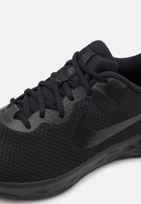 Scarpa atletica nera con una tomaia in mesh traspirante, dettagli in materiale sintetico liscio e lacci neri piatti, con un logo ben visibile sul lato.