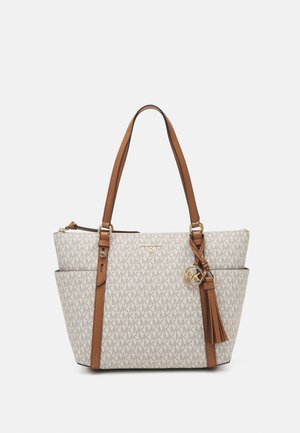 Beige Michael Kors shopper med brune læderstropper, all-over MK logo mønster, guldfarvet hardware og en kvast charm, der hænger foran.