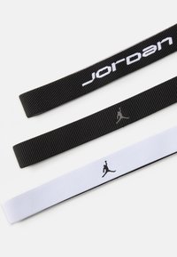 Trys elastingos dirželiai: juodas su "Jordan" tekstu, juodas su logotipu ir baltas su logotipu. Tekstūruotas, tvirtas audinys; skirtas sportiniam naudojimui.