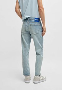 Jasnoniebieskie dżinsy o prostym kroju, pięć kieszeni i niebieska łatka z logo HUGO z tyłu. Noszone z jasnymi trampkami.