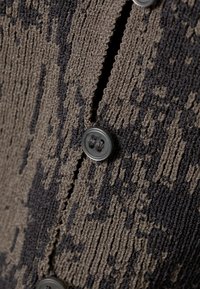 Primo piano di tessuto lavorato a maglia con motivi grigio scuro e nero, con un bottone cucito vicino a una asola.