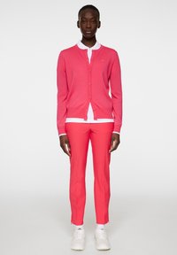 Cardigan rosa, camicia bianca sotto e pantaloni rosa. Sneakers bianche. Il cardigan ha bottoni e una vestibilità aderente; i pantaloni sono affusolati alle caviglie.