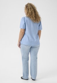 Haut bleu clair à manches courtes avec une finition texturée, associé à un jean en denim clair. Jean à coupe droite avec peu de détails matériels visibles.