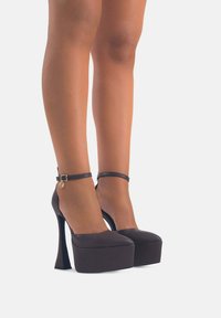 Tacchi alti neri a piattaforma con punta affilata e cinturino alla caviglia. Realizzati in un materiale liscio con una finitura lucida e un design con tacco spesso.