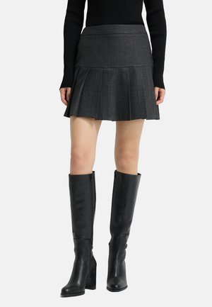 Mini-jupe plissée grise avec une finition texturée, associée à des bottes en cuir noir montantes avec un talon bloc et une fermeture éclair sur le côté.