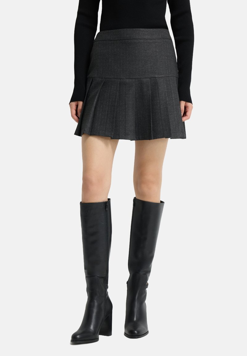 Grå plisseret mini nederdel med en tekstureret finish, parret med knæhøje sorte læderstøvler med blokhæl og lynlås i siden.