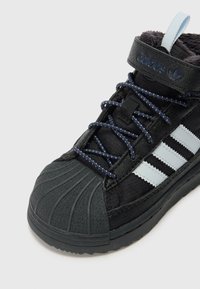 Sapatilha alta preta com biqueira de borracha, tecido texturizado e atacadores azuis. Apresenta riscas e logótipo da Adidas em azul claro na tira.