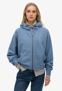 Blauwe rits hoodie gemaakt van zachte fleece, met een capuchon met trekkoord, voorzakken, ribgebreide manchetten en een lichtgestreept shirt eronder.