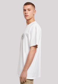 White cotton t-shirt with a round neckline and short sleeves. Features a circular graphic design on the left chest area.
