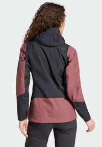 Veste résistante à l'eau avec un design en blocs de couleurs noir et bordeaux, panneaux texturés et une capuche ajustée. Tissu léger avec des manches longues.
