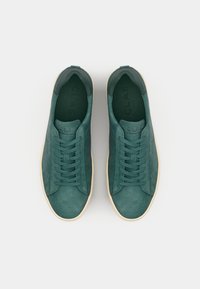 Green suede sneakers with a smooth texture, rounded toe, flat laces, and a contrasting cream sole. Embossed logo on the tongue.