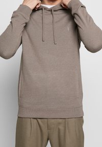 Felpa con cappuccio color marrone chiaro, realizzata in tessuto morbido, dotata di una tasca a marsupio, polsini a coste e un piccolo logo sul petto.